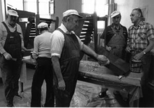 old black and white photo of group of men wearing work clothes in workshop setting