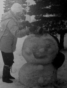 old black and white photo of person in winter clothes standing next to snow sculpture