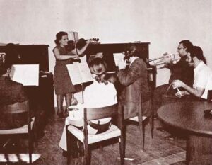 old black and white photo of group of people sitting or standing playing various musical instruments