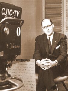 old black and white photo of man in suit facing television camera, 1950s look