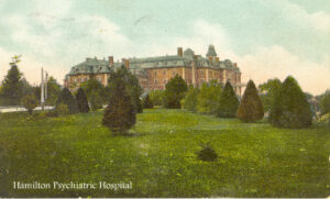 large imposing old brick building on hill with shrubs and grass in front