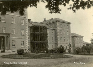 black and white photograph of wing of old brick institutional building, driveway and gardening in front