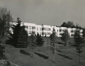 White building up a sloping lawn with small trees.