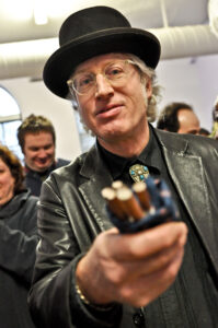man with glasses and black hat holding out a pack of cigarettes