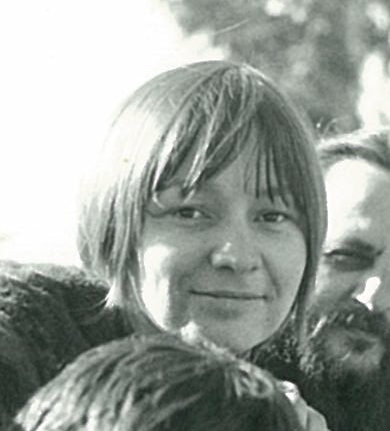 3 young women and a man with long hair and a beard all sitting together with the woods behind.